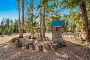 A wooden climbing structure with a green roof, surrounded by trees and a forested area.