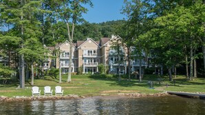 A lakeside property with a large building featuring multiple balconies and a grassy lawn.