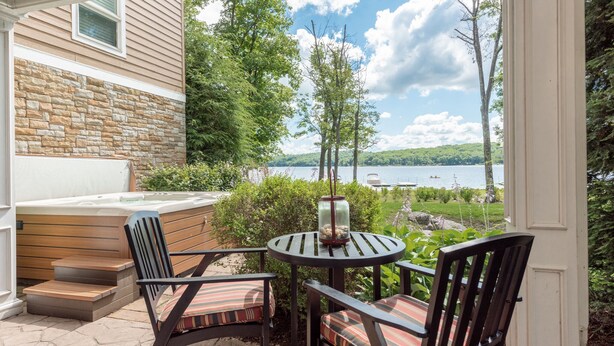 A patio with a hot tub, wooden steps, and two chairs with striped cushions.