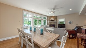 A dining area with a wooden table and white chairs, a fireplace, and a TV mounted on the wall.