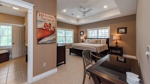 A bedroom with a bed, bedside lamps, a desk, and a chair. There is a ceiling fan and a window with blinds.