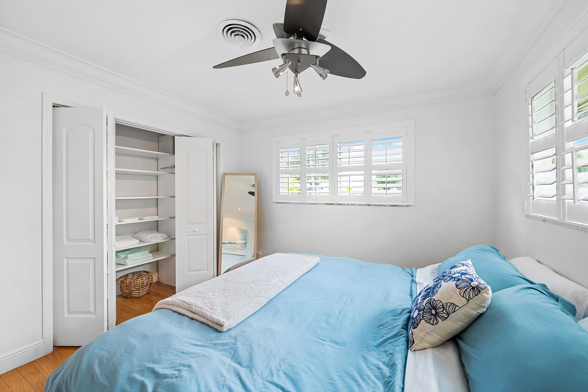 A bedroom with a bed, a ceiling fan, a window with blinds, and a wardrobe.