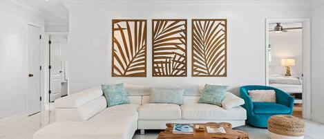 A modern living room with a white sectional sofa, a blue armchair, a wooden coffee table, and a decorative wall panel.