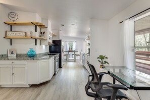 A modern kitchen with white cabinetry, a glass-top dining table, and a view of the outdoors through a large window.