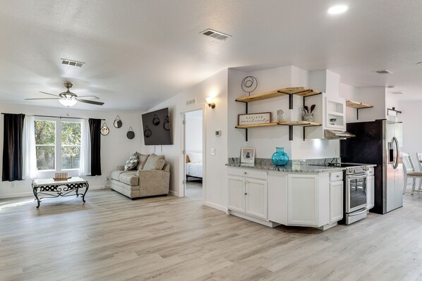 A spacious living area with a ceiling fan, a sofa, a coffee table, and a kitchen with white cabinets and a built-in oven.