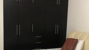 Une chambre avec une grande armoire noire, un lit avec une literie blanche et un oreiller rouge.