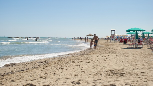 Une plage où l’on voit des gens se promener le long du rivage, des parasols et des chaises de plage.