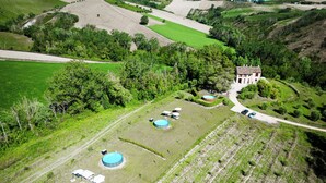 Vue aérienne d’un domaine rural comprenant une grande maison, plusieurs piscines et de vastes champs verdoyants.