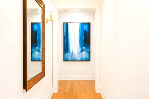 Ein Flur mit zwei gerahmten abstrakten Gemälden an der Wand, Holzboden und einem Spiegel links.