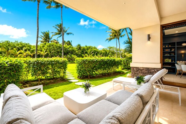 A modern outdoor seating area with a view of a well-maintained garden and palm trees.