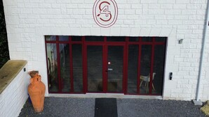 Un bâtiment à l’extérieur en briques blanches, avec une porte à cadre rouge et un grand logo circulaire au-dessus de la porte.