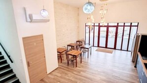 Un espace repas avec des tables et des chaises en bois, une chaise rouge et un escalier menant à une autre pièce.