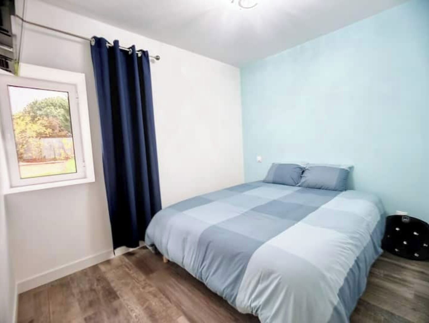 Une chambre à coucher avec un lit, une fenêtre avec un rideau et un tableau encadré au mur.