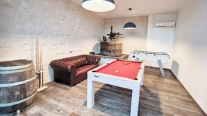 Une pièce équipée d’une table de billard, d’un canapé en cuir, d’un tonneau en bois et d’une table de ping-pong.