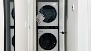 Een wasserette met twee gestapelde wasmachines, een deur met een hendel, en een spiegel aan de linker muur.