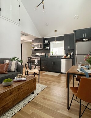 A modern kitchen with dark cabinets, a stainless steel refrigerator, and a dining area with a table and chairs. - The Historic Bell House Hygge Retreat (Andover)