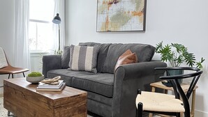 Een moderne woonkamer met een grijze bank, een houten salontafel, een zwarte fauteuil en een groot abstract schilderij aan de muur.