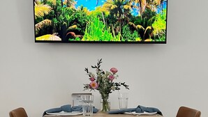 Een eettafel met twee stoelen, een vaas met bloemen en twee glazen op een houten tafel met een zwart metalen frame.