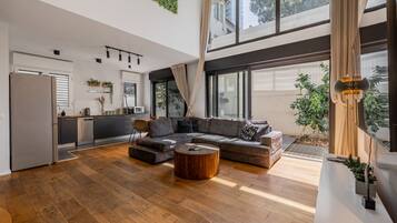 Uma sala de estar ampla com um sofá modular grande, uma mesa de centro de madeira e uma cozinha ao fundo.