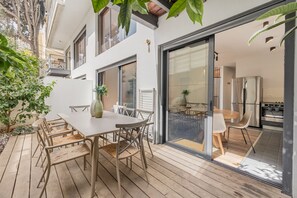 A modern patio with a dining table and chairs, a potted plant, and a view into the kitchen.
