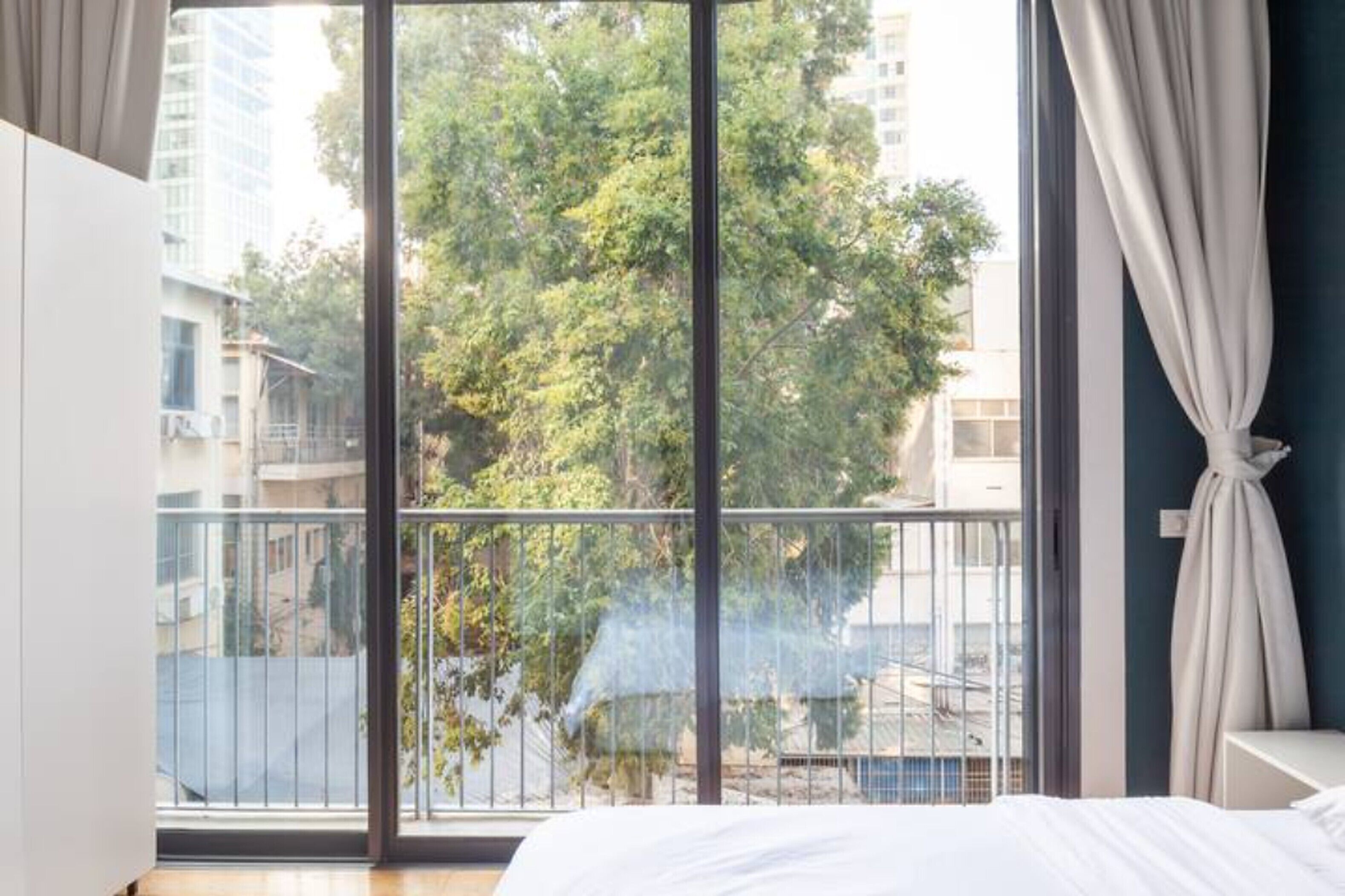 Um quarto com uma janela grande, uma cama e uma cortina.