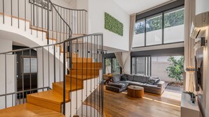 Ein modernes Interieur mit einer Holztreppe, einem Wohnbereich mit Sofa und Couchtisch sowie großen Fenstern.