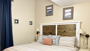 Une chambre à coucher avec un lit, une table de chevet, une lampe et des tableaux encadrés accrochés au mur.