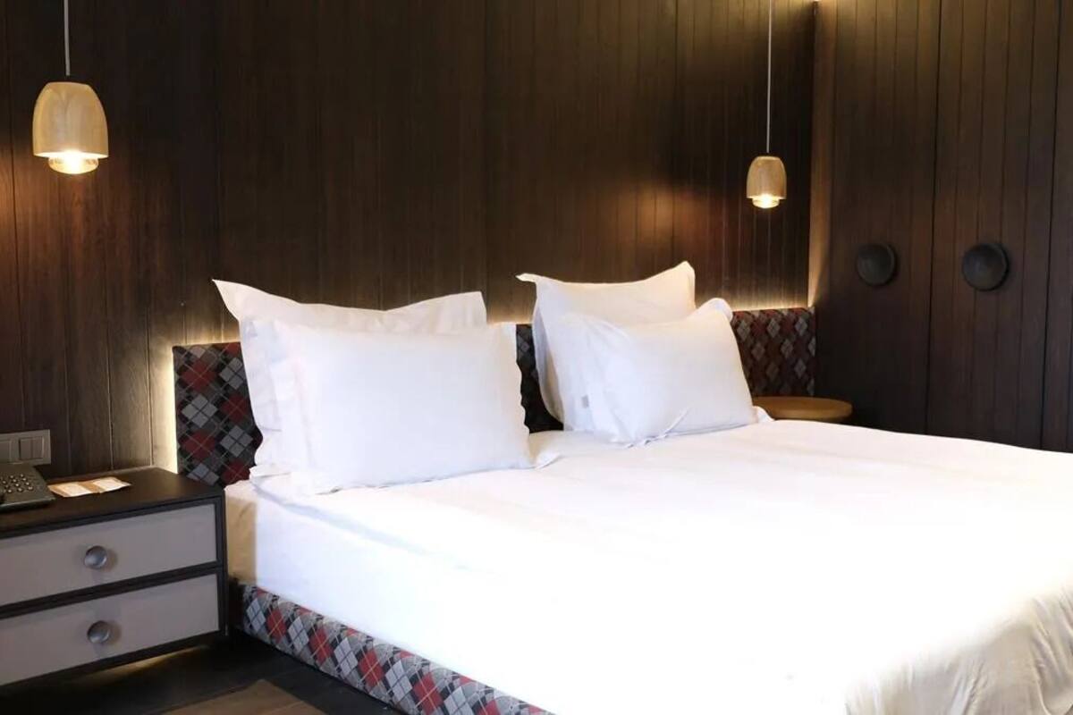 A neatly made bed with white linens and two pillows, a bedside table with a lamp, and a patterned wall.