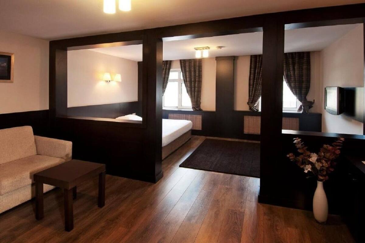 A hotel room with a sofa, a small table, a bed, a TV, and a vase with flowers.