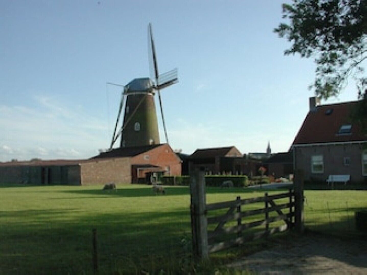 En vindmølle med et traditionelt design, omgivet af en græsplæne og et træhegn.