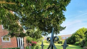 A metal fence with ornamental designs, a well-maintained lawn, and a brick building in the background. - Cozy farmhouse, Zeeland, original, large garden, wallbox 22KW (Gapinge)