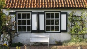 A white building with a tiled roof and black-framed windows. There is a white bench in front of the building. - Cozy farmhouse, Zeeland, original, large garden, wallbox 22KW (Gapinge)
