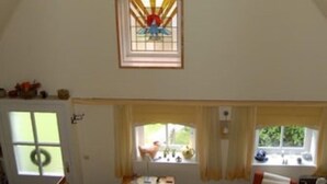 A spacious room with a high ceiling, a dining area with a table and chairs, and a window with curtains. - Comfortable apartment in a cozy farmhouse for 2-3 persons 22KW Wallbox (Gapinge)
