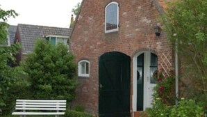 A brick building with a tiled roof, a white bench, and a green lawn. - Comfortable apartment in a cozy farmhouse for 2-3 persons 22KW Wallbox (Gapinge)