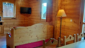 A wooden cabin room with a bed, a table, a lamp, a TV, and a microwave.