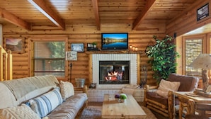 A log cabin interior with a fireplace, wooden furniture, and a television mounted above it. - Bear Kub Kabin + Games + 1 Block to Snow Summit! (Big Bear Lake)