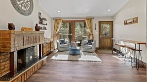 Una sala de estar con chimenea, dos sillones, una mesa de centro y una mesa de comedor.