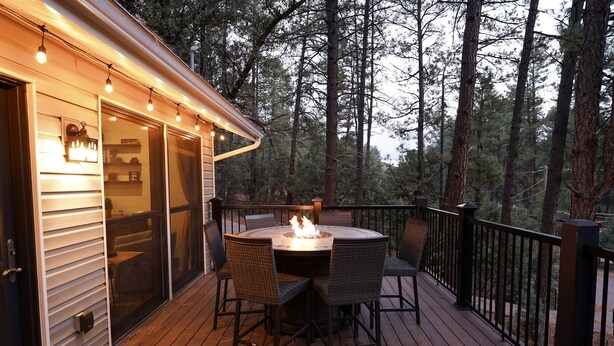 Una terraza al aire libre con una mesa redonda y sillas, una chimenea y vistas a un bosque.