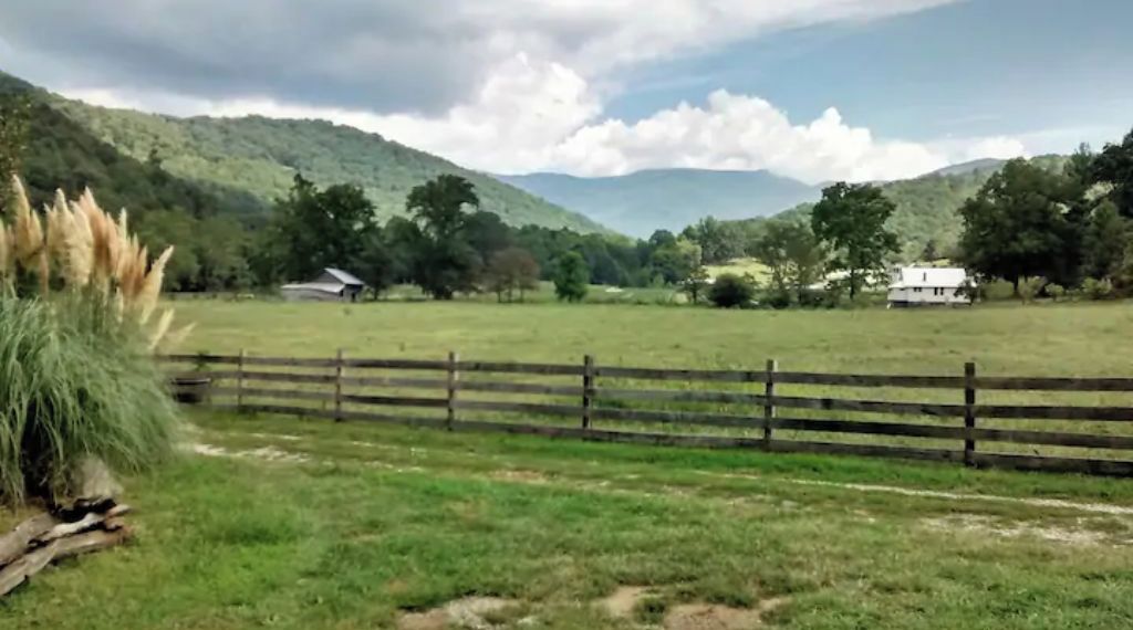 A rural landscape with a wooden fence, grassy fields, and a few scattered trees.
