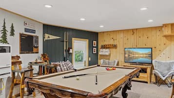 Uma mesa de bilhar em um ambiente com paredes de madeira, uma televisão e uma placa com a inscrição 'LAKE LIFE'.