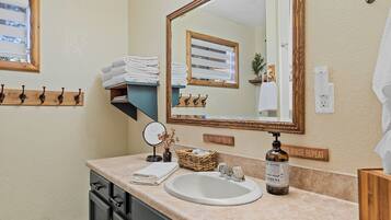 A bathroom with a sink, mirror, towel rack, and a soap dispenser.