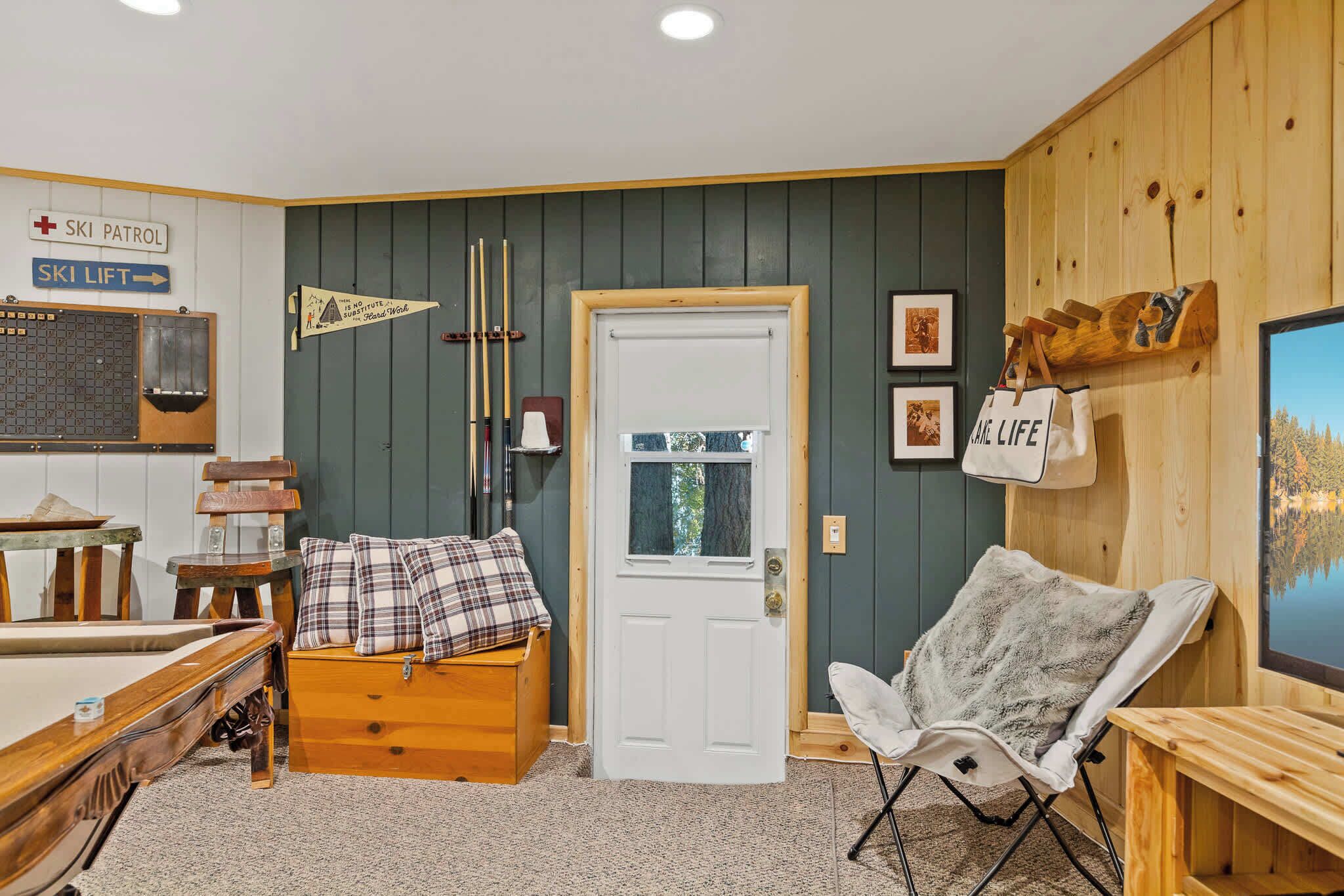 Um quarto aconchegante com mesa de bilhar, um banco de madeira com almofada xadrez, uma porta branca e um aviso de teleférico.