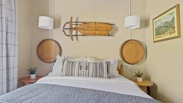 Un dormitorio con cama, dos mesitas de noche, un tronco de madera montado en la pared, dos lámparas de pared y un cuadro con paisaje enmarco.