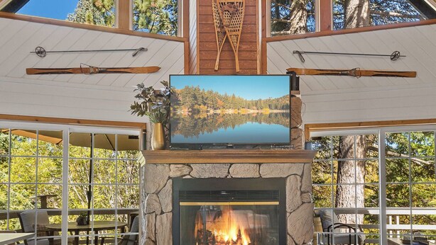 A spacious living room with a stone fireplace, a large flat-screen TV, and a ceiling fan.