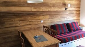 Una habitación acogedora con pared de madera, una mesa de madera con sillas, un sofá con cojines a rayas y una lámpara colgante.