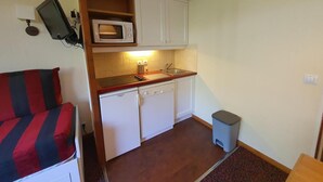 Una kitchenette compacta con microondas, pileta y heladera pequeña.