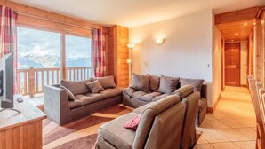 Una sala de estar acogedora con un sofá modular, un televisor y vistas a montañas a través de amplios ventanales.
