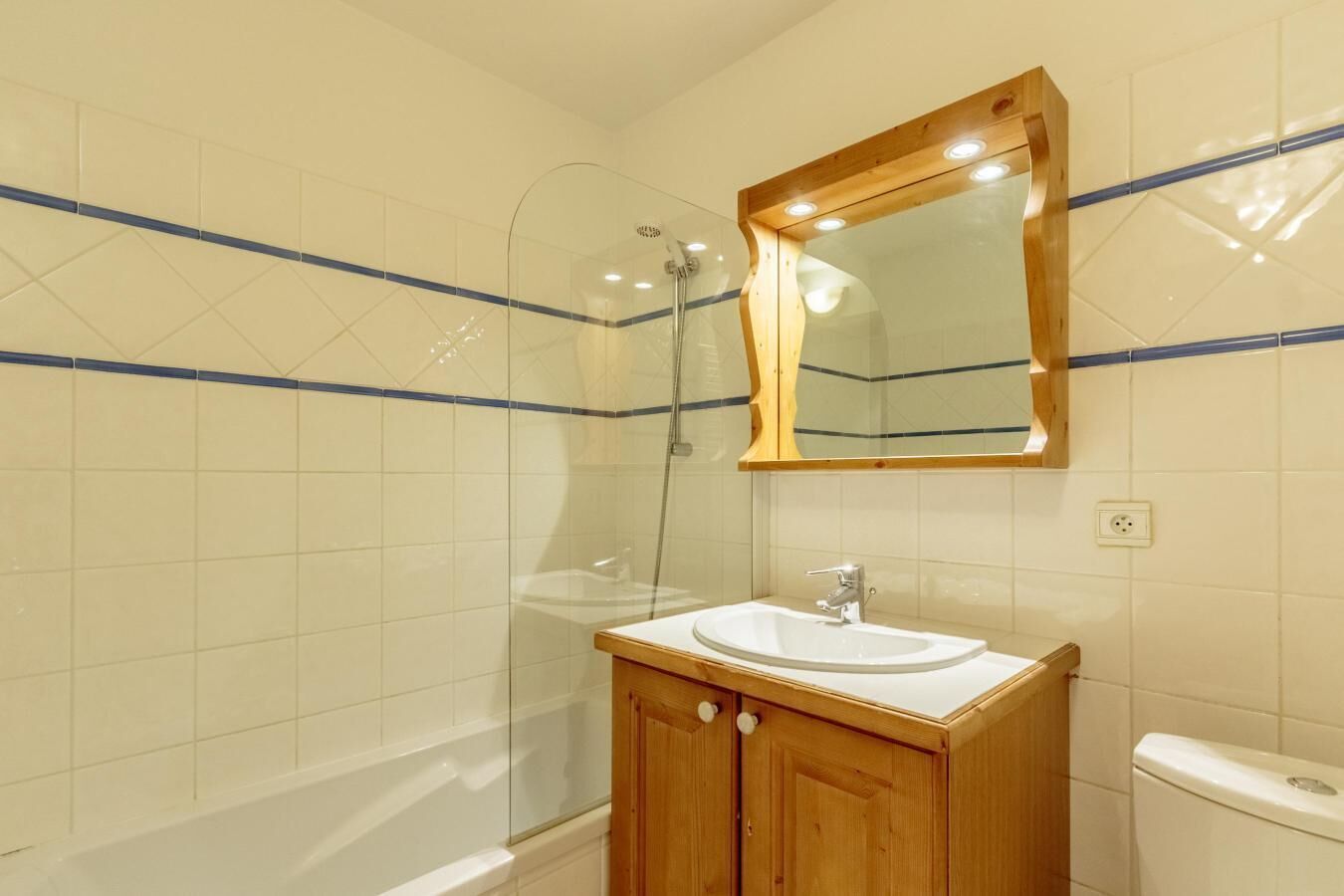 A bathroom with a glass shower enclosure, a wooden vanity with a sink, and a mirror above the vanity.