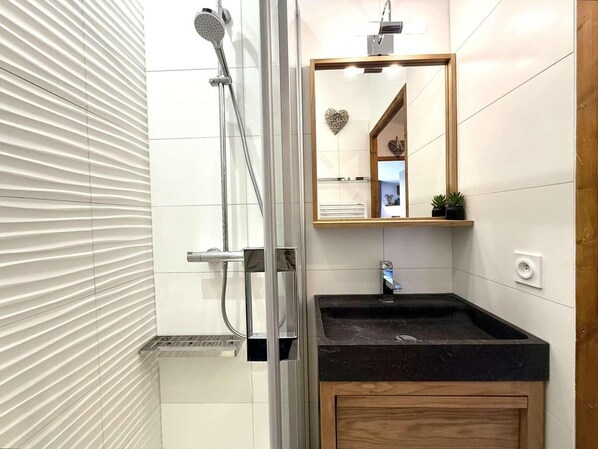 Une salle de bain avec une douche à parois de verre, un lavabo avec un meuble en bois et un miroir orné d’un motif en forme de cœur.