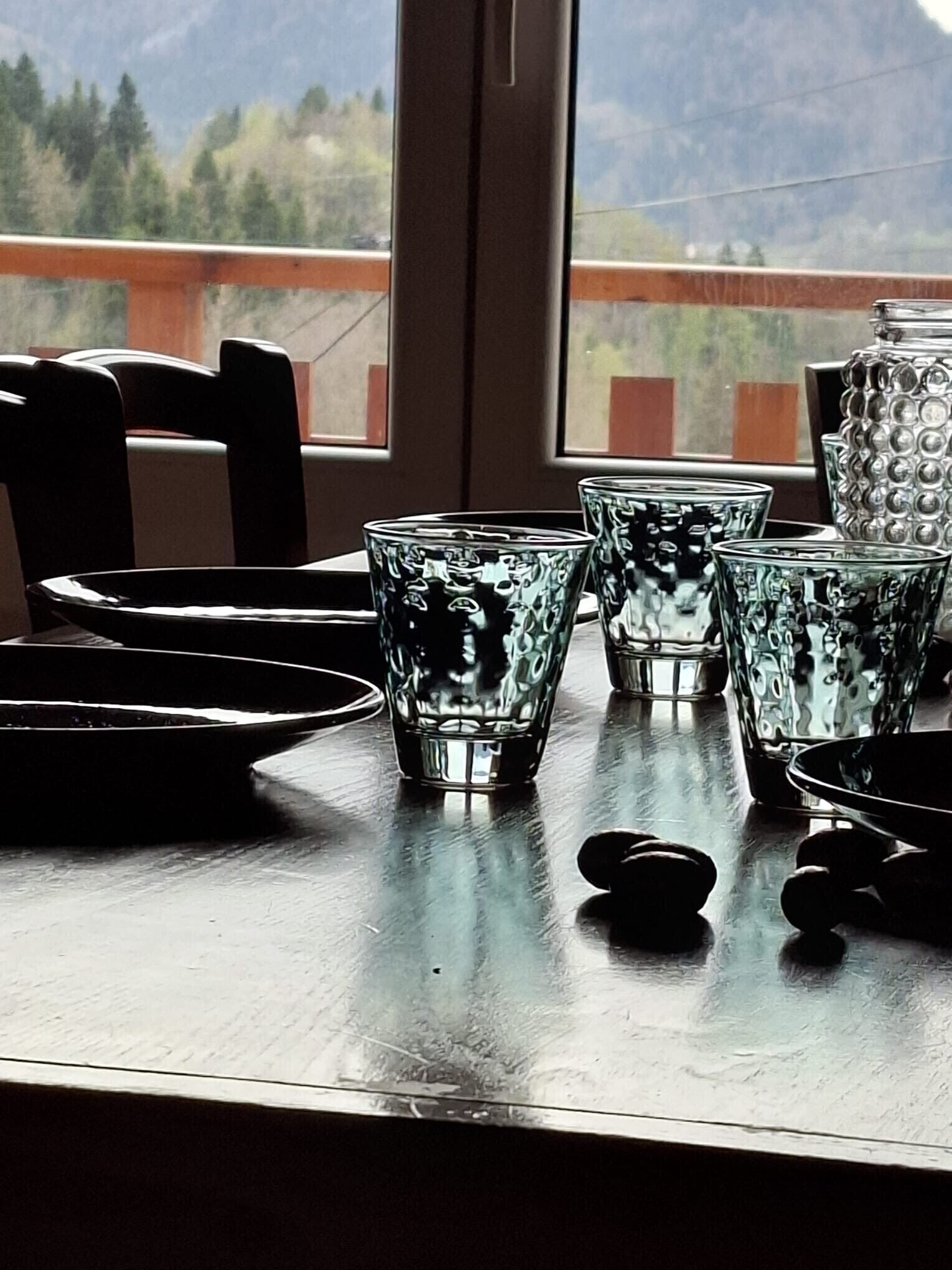 Una mesa con cristalería transparente y un recipiente metálico, frente a una ventana con vista a la montaña.